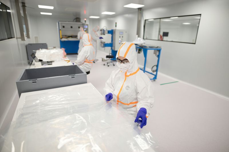Workers in hooded white coveralls with taped seams, masks and nitrile gloves in a cleanroom