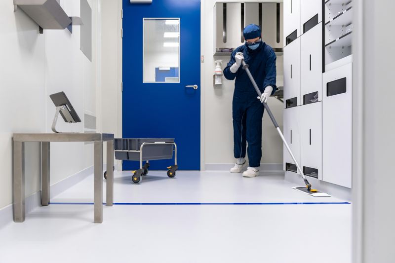 Cleanroom worker in a bouffant cap, mask, gloves and shoe covers mopping a sterile room
