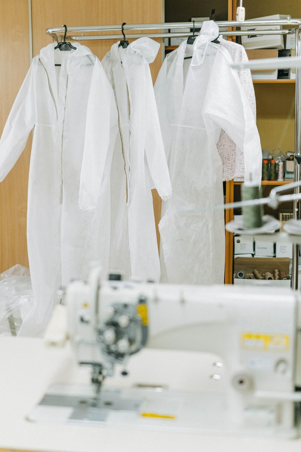 Disposable white coveralls hanging on a rack beside a sewing machine