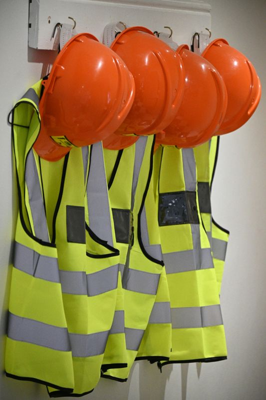 Orange hard hats and hi-vis yellow safety vests hanging on a wall